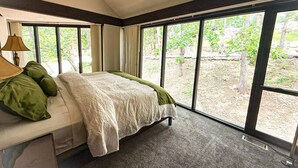 A bedroom with a large window, a bed with green pillows, and a lamp on a bedside table.
