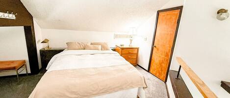 A bedroom with a bed, bedside table, lamp, and a door.