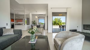 Una sala de estar moderna con sofá, sillón y una mesita de centro. Se observa un comedor con mesa y sillas, y una cocina al fondo.
