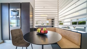 Una cocina moderna con electrodomésticos integrados, una mesa de comedor redonda con frutero y una zona de estar con vistas.