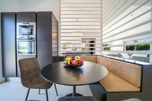 A modern kitchen with built-in appliances, a round dining table with a fruit bowl, and a seating area with a view.