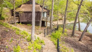 A wooden cabin with a balcony, surrounded by trees and a lake.