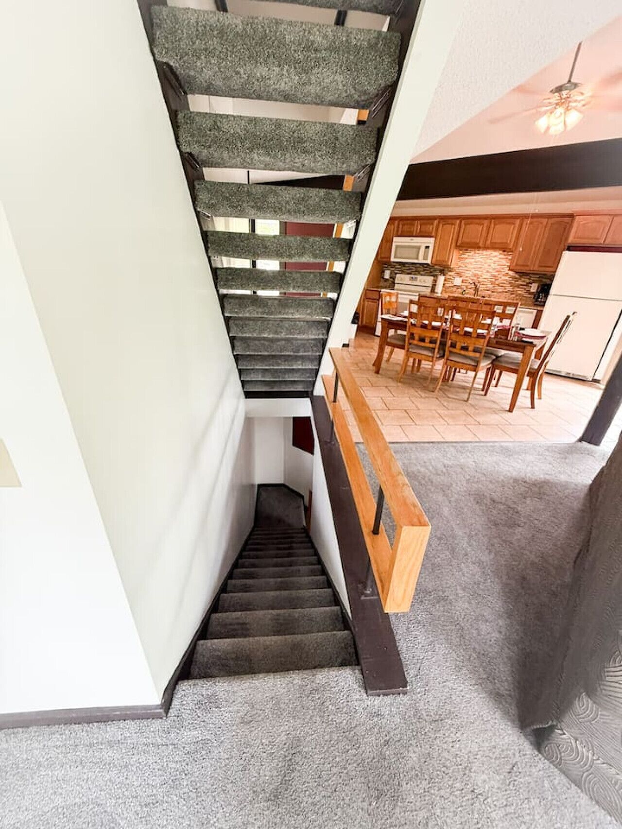 Una escalera moderna con alfombra gris y barandilla de madera que lleva a un comedor con sillas y mesa de madera.