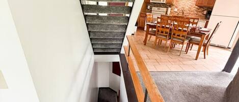 Una escalera moderna con alfombra gris y barandilla de madera que lleva a un comedor con sillas y mesa de madera.