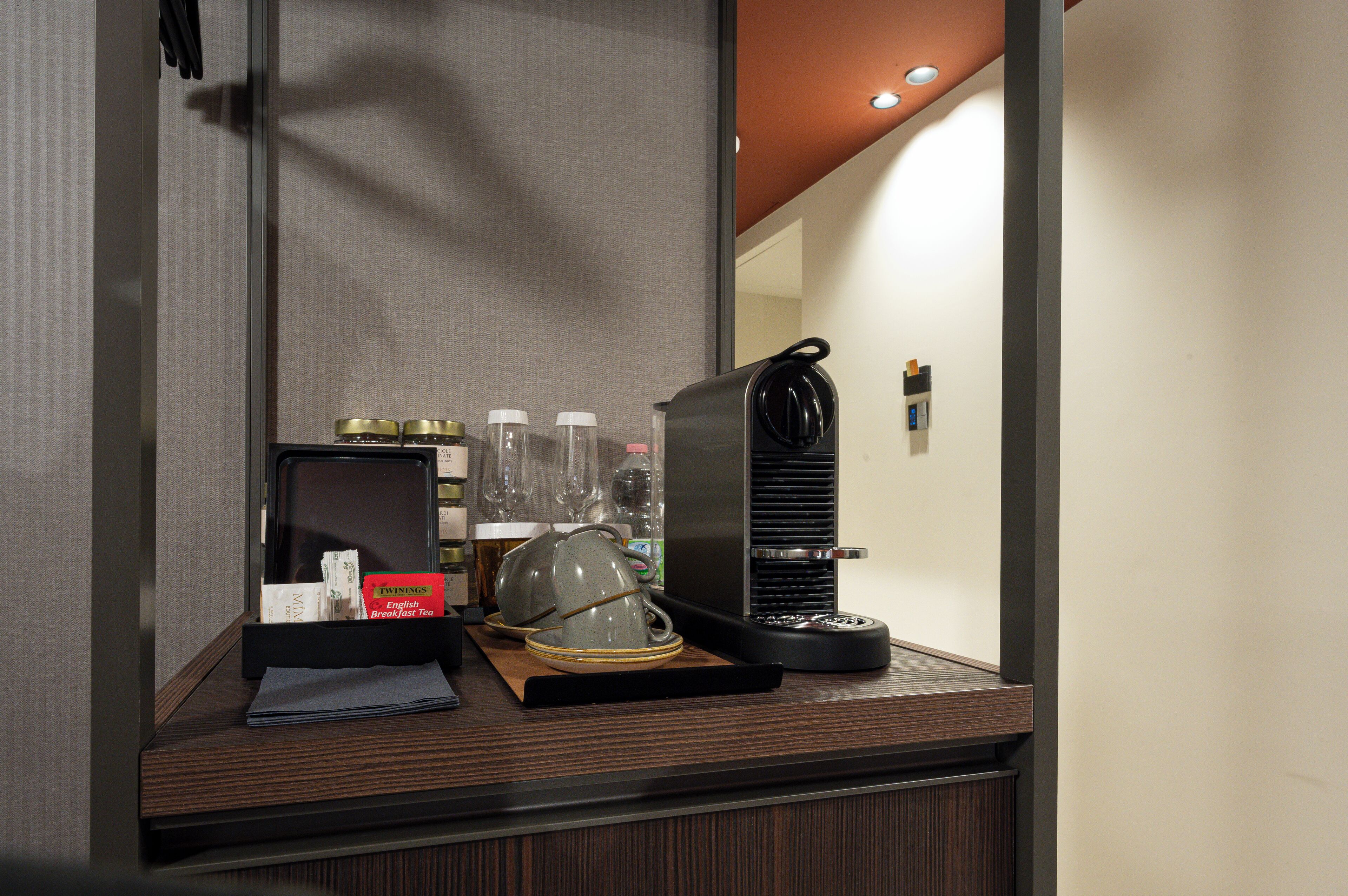 A hotel room's breakfast area with a coffee maker, tea kettle, and breakfast items on the counter.