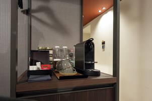 Zona de desayuno en una habitación de hotel, con cafetera, tetera y alimentos para el desayuno en la encimera.