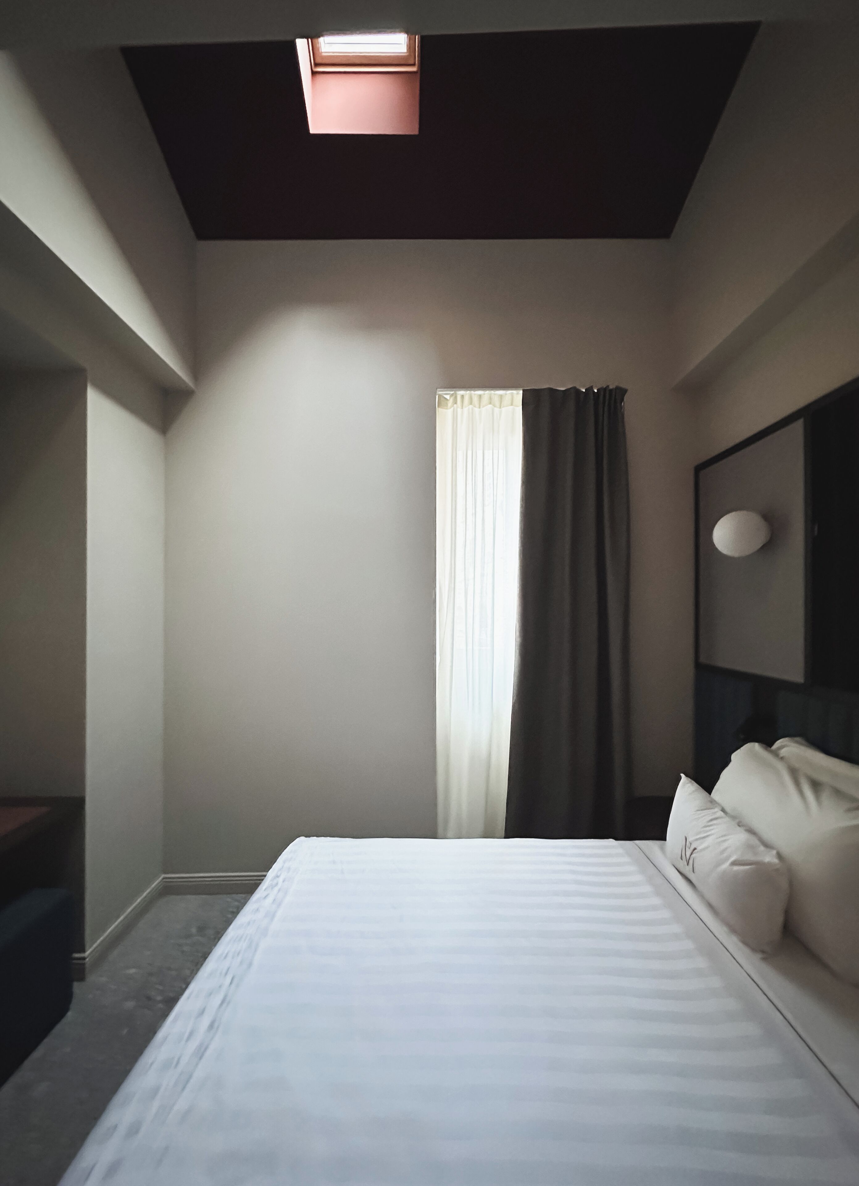Una camera da letto con un letto, una finestra con tende, una lampada a soffitto e uno specchio fissato al muro.