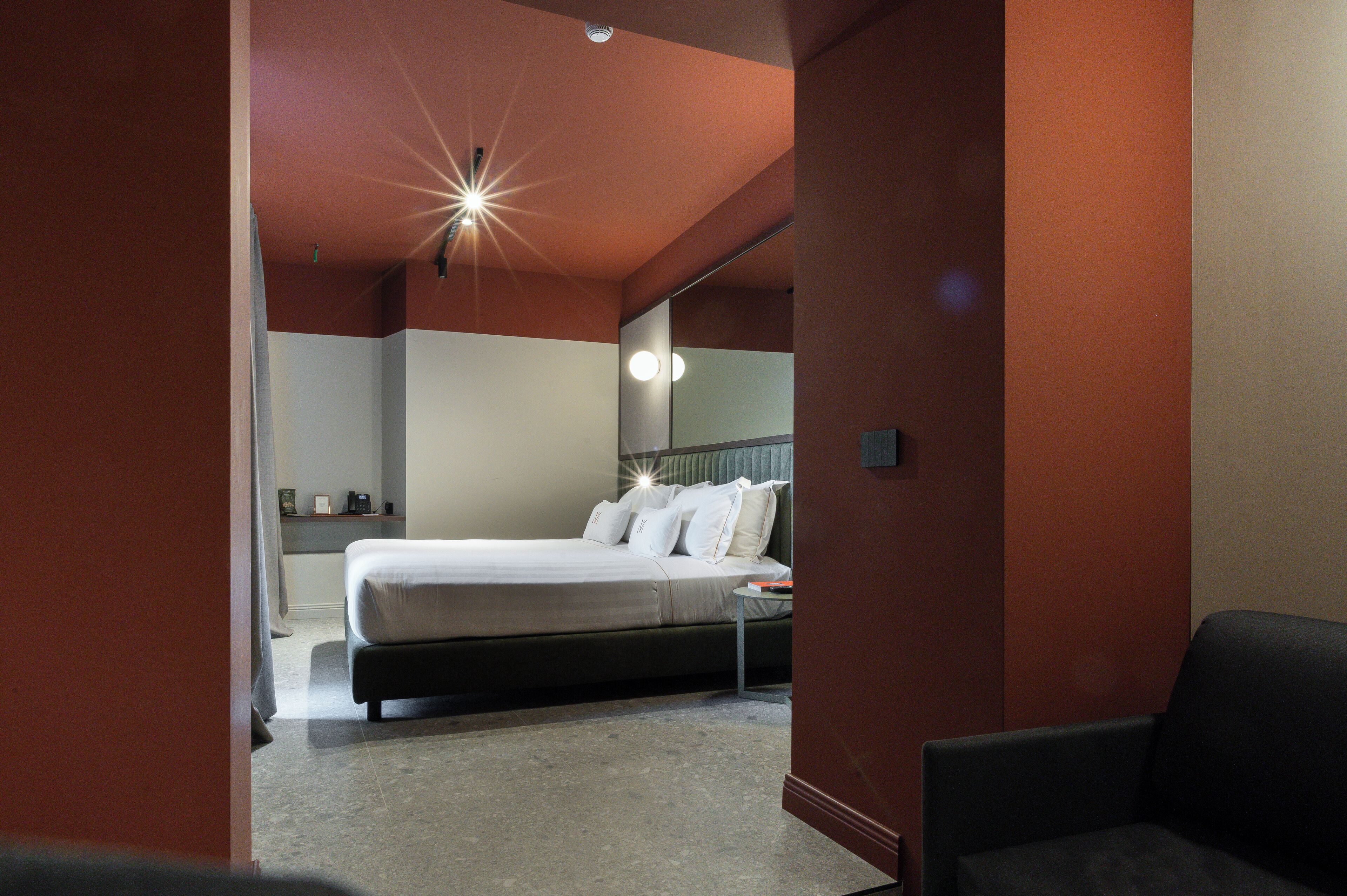 A modern hotel room with a large bed, a bedside table, a mirror, and a ceiling light fixture.