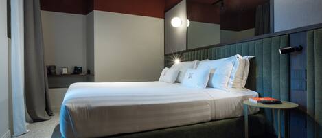 A neatly made bed with pillows, a bedside table with a book, and a mirror on the wall.