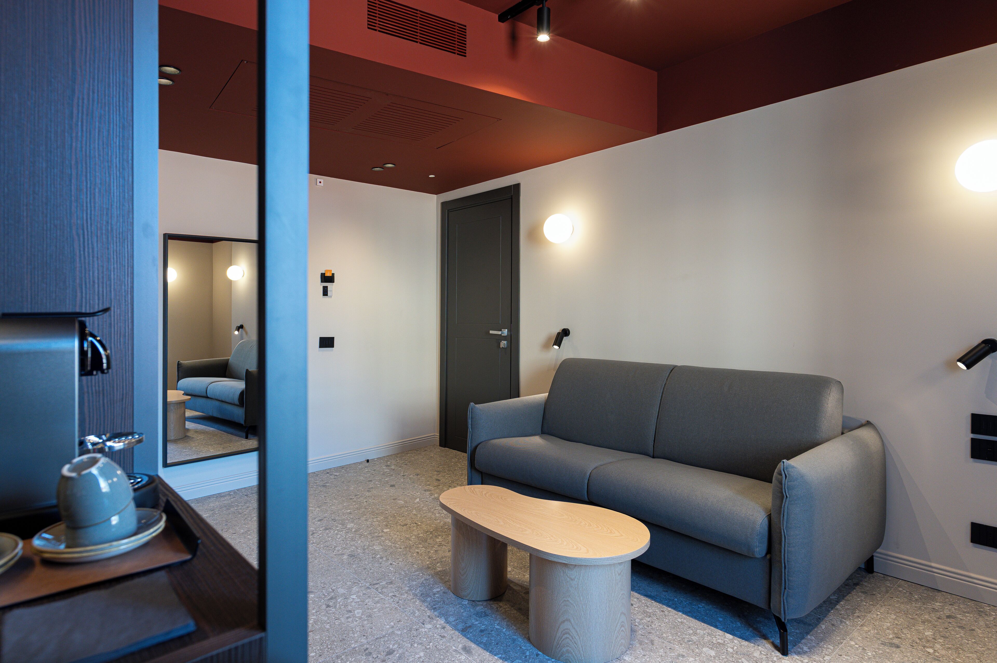 A modern living room with a grey sofa, a wooden coffee table, and a small side table with a kettle and cups.