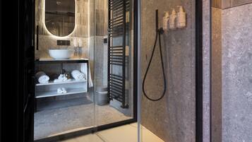 Un baño moderno con ducha envuelta en vidrio, un espejo ovalado grande, un lavabo blanco y un perchero para toallas.