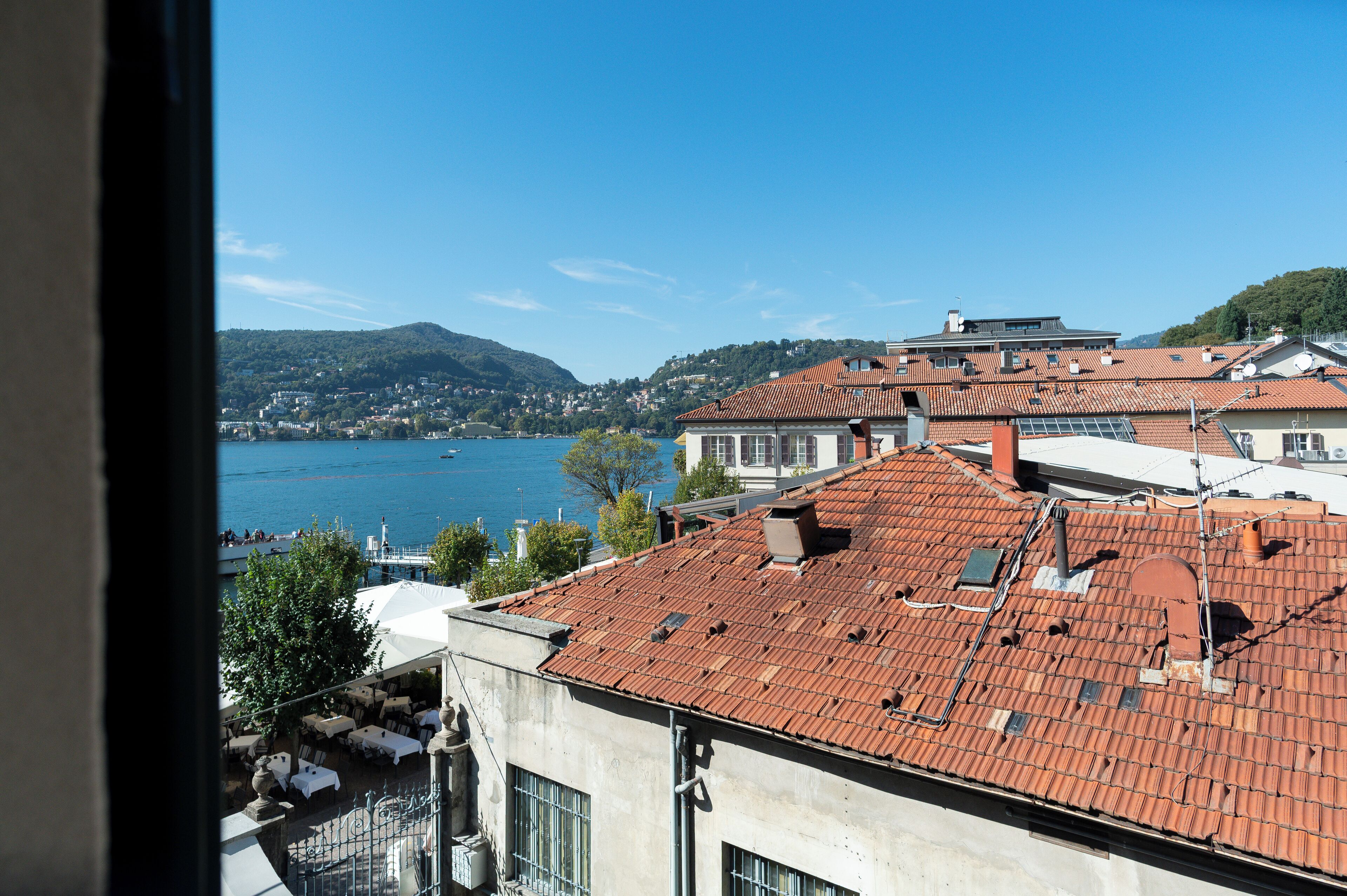 A coastal town with terracotta-roofed buildings, a view of the sea, and a hillside in the background.