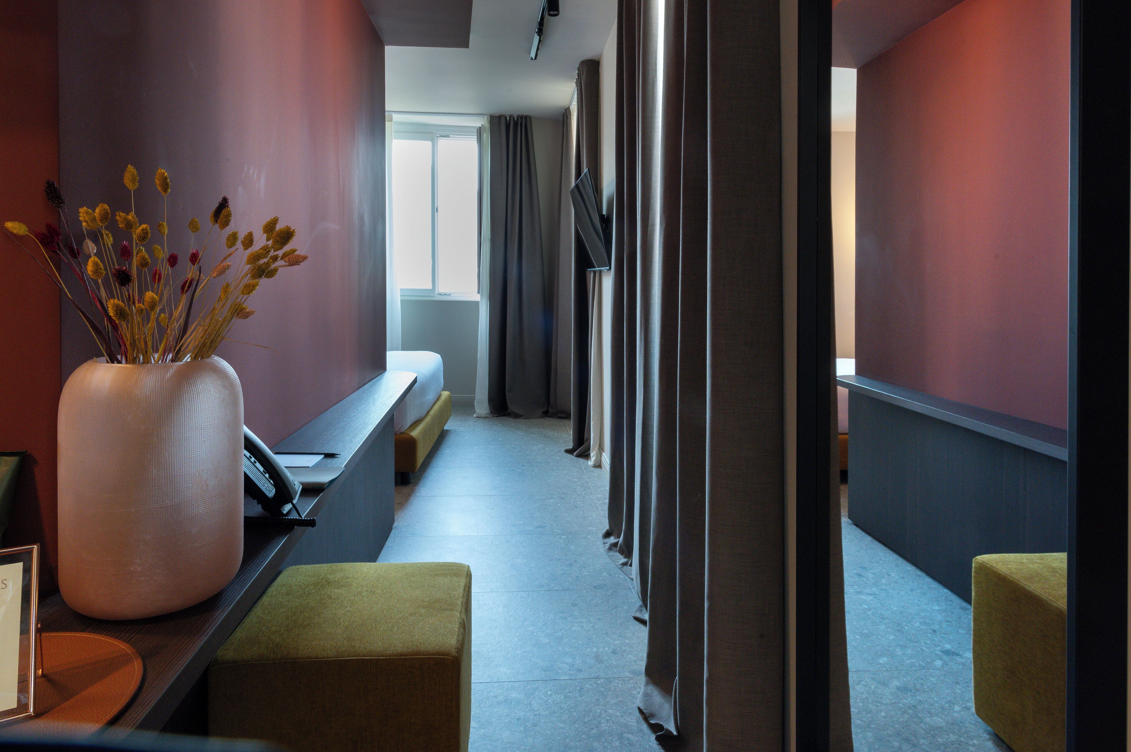 Eine moderne Hotelhalle mit einer Rezeption, einer Vase mit Trockenblumen, einer Bank und Blick auf den Flur.