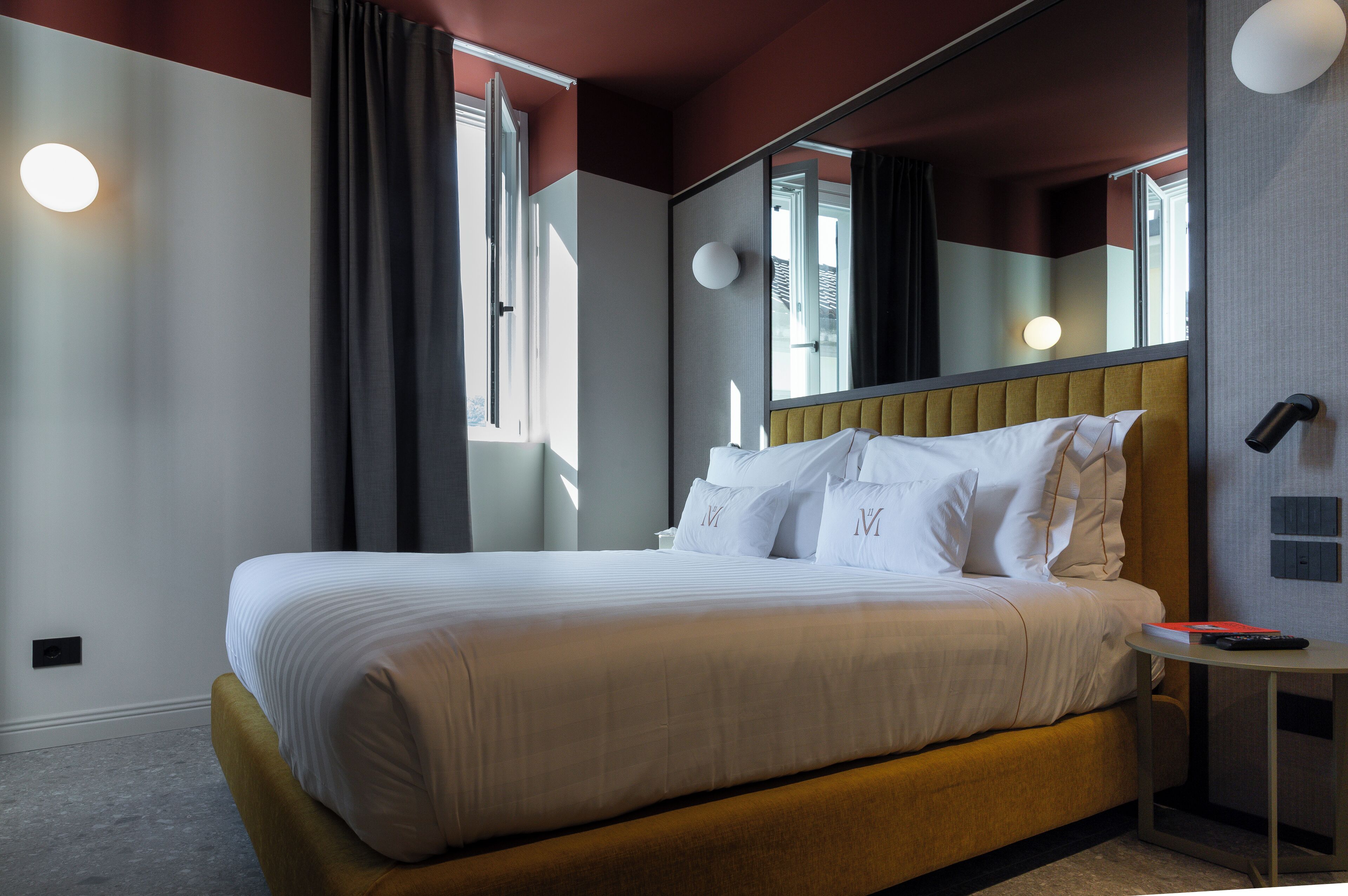 A neatly made bed with white linens and pillows, a bedside table with a remote control, and a large mirror above the bed.