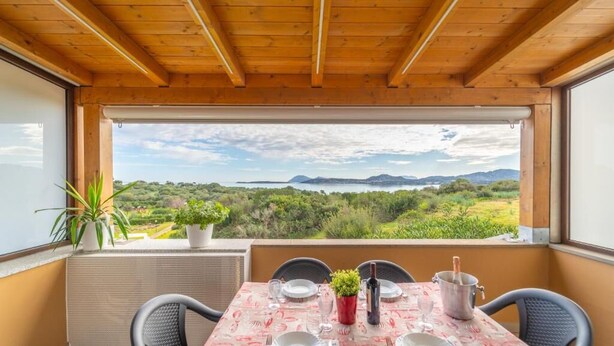 A dining area with a table set for two, overlooking a scenic landscape with mountains and greenery. - SMERALDA Blue Sky (Portisco)