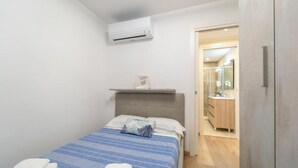 A small, modern bedroom with a bed, a bedside table, and an air conditioning unit. - SMERALDA Blue Sky (Portisco)