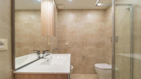 Une salle de bain moderne avec un grand miroir, deux lavabos, des toilettes et une douche à parois de verre.
