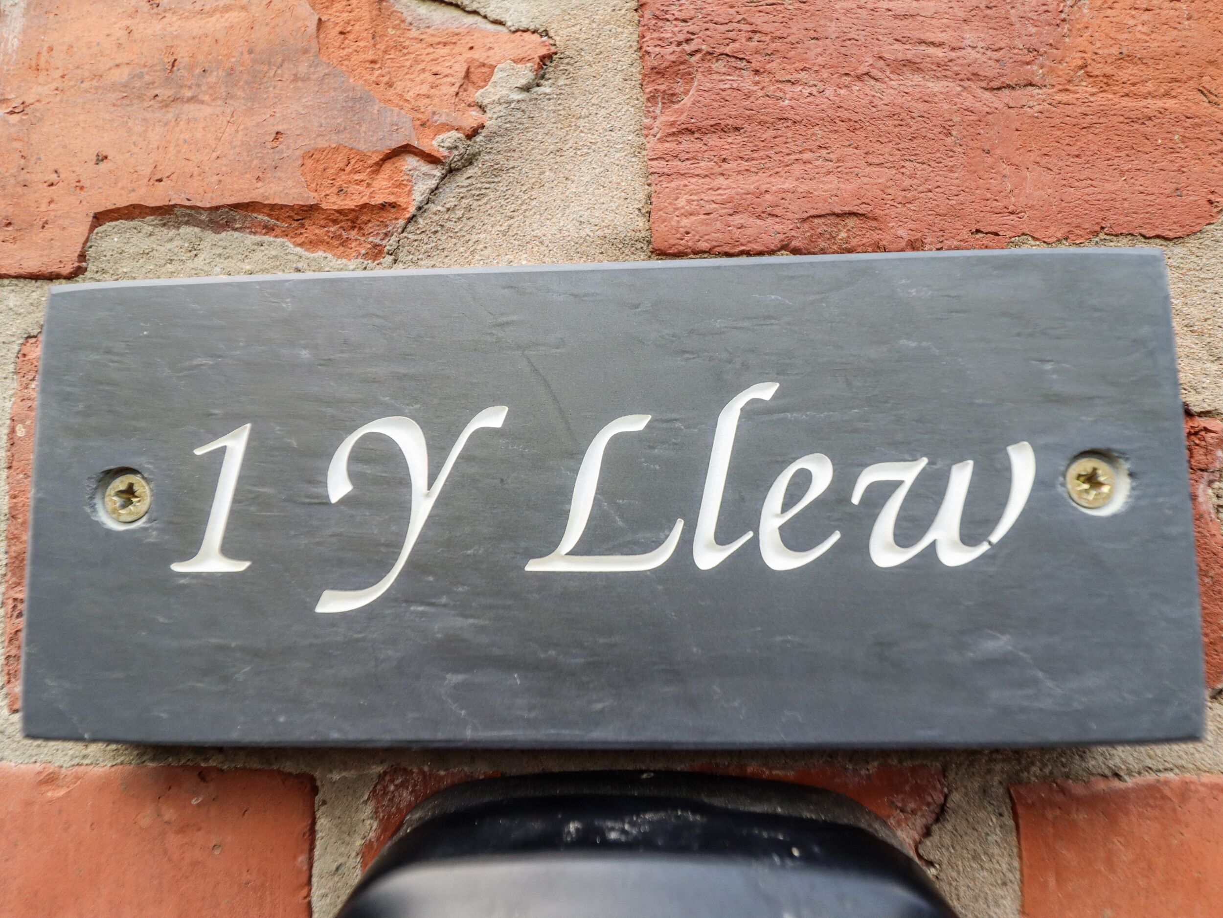 Une plaque en ardoise portant le numéro de maison « 1Y Llew », fixée sur un mur de briques.