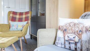 A cozy room with a yellow armchair, a plaid throw pillow, a large bed with a dog-themed pillow, and a wooden wardrobe.