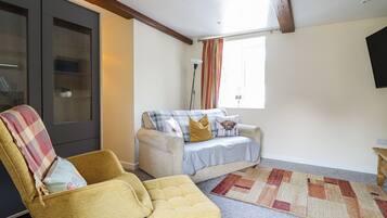 A cozy living room with a sofa, armchair, and ottoman, a large cabinet, and a patterned rug.