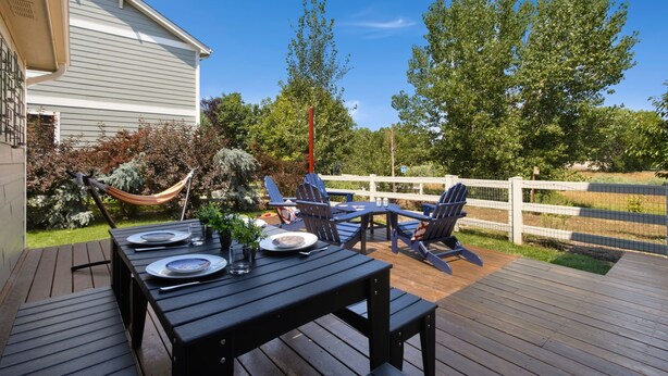 Une terrasse extérieure avec une table en bois, dressée pour deux personnes, entourée de chaises Adirondack.