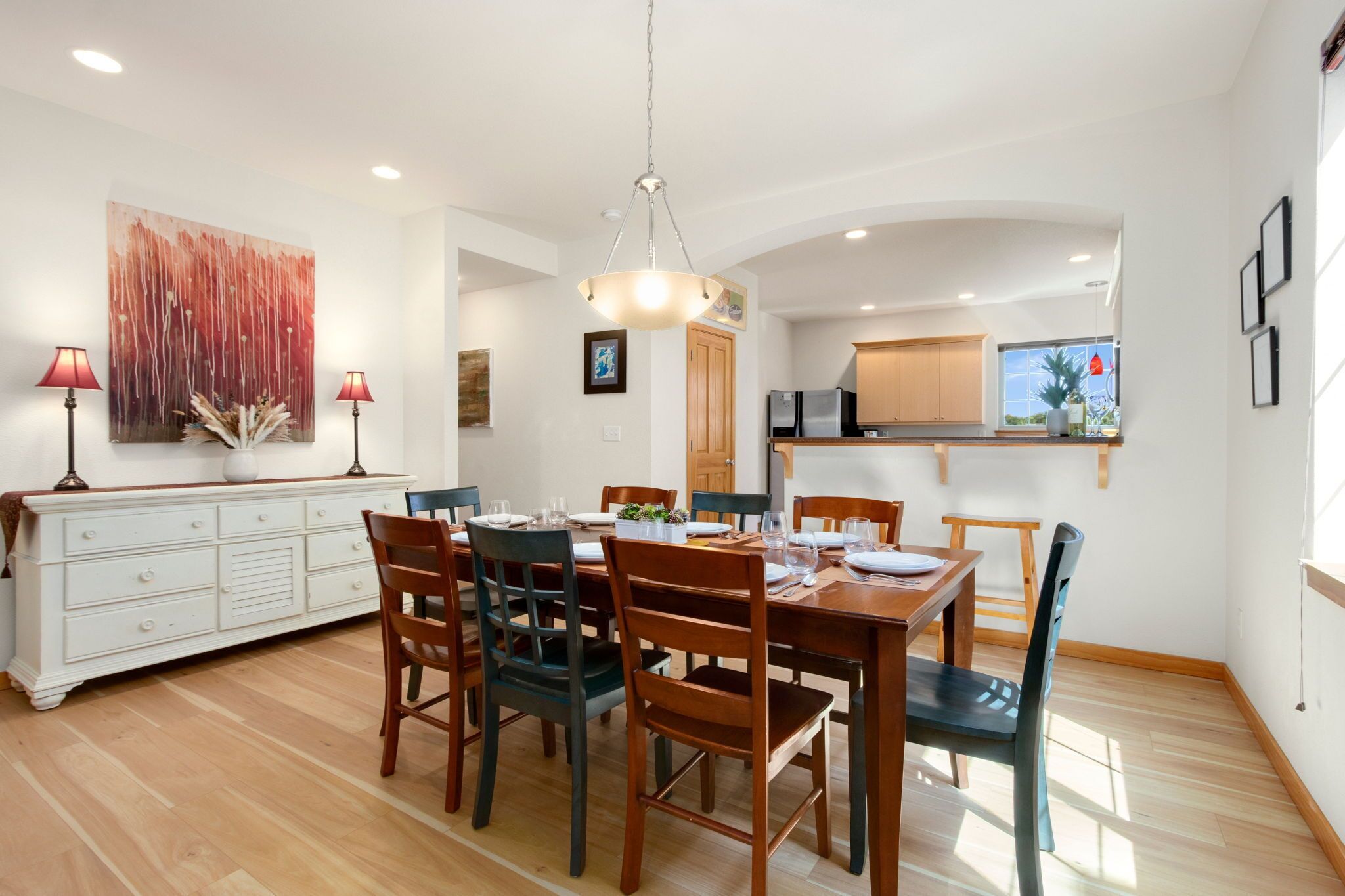 A dining area with a wooden table and chairs, a white cabinet, and a painting on the wall.