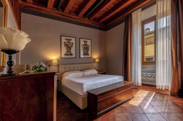 A bedroom with a bed, bedside tables, a dresser, a lamp, and two framed vases on the wall. - Antica Dimora De Benci (Florence)