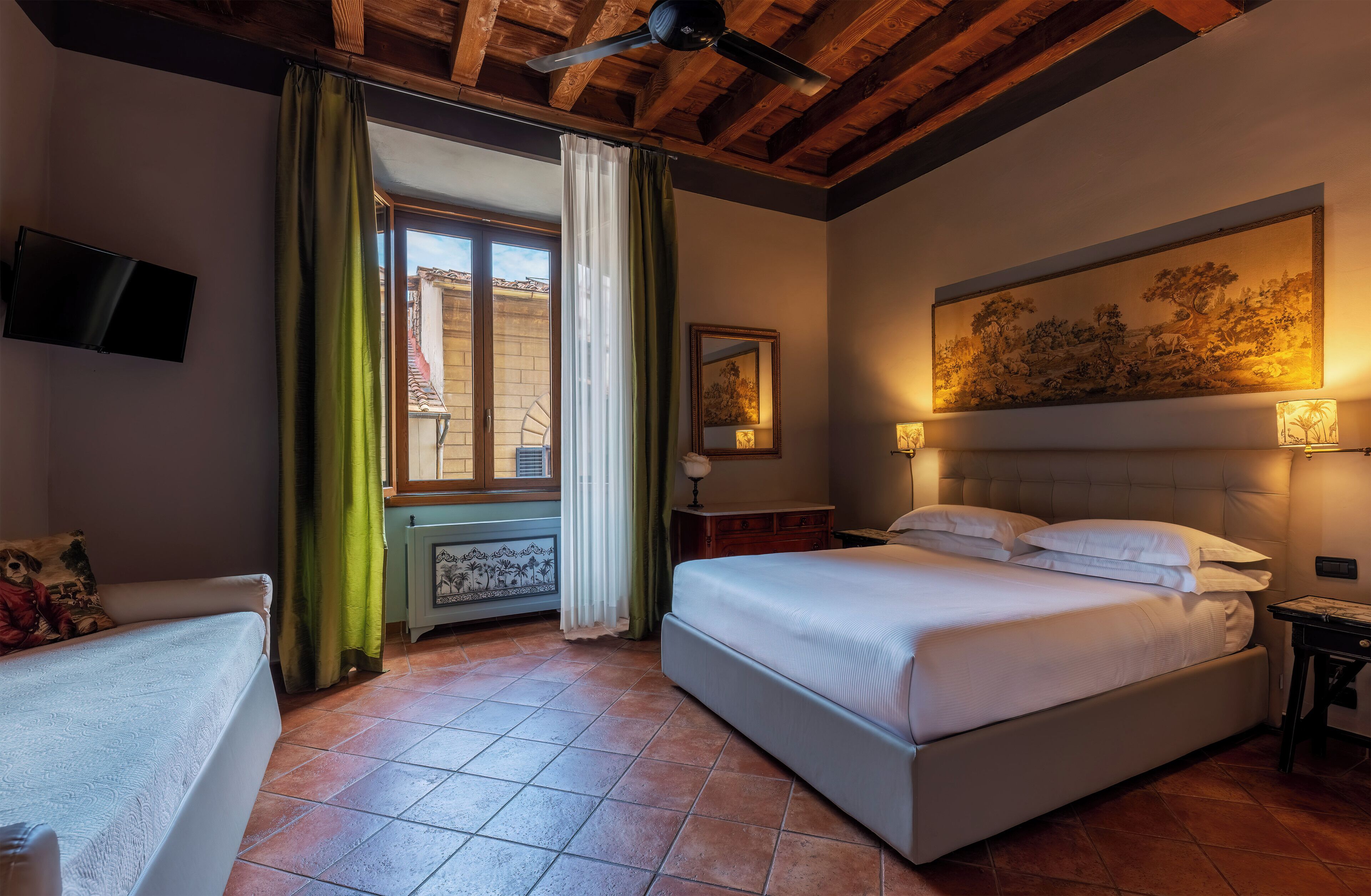 Une chambre à coucher avec un lit, une télévision, un tableau et une fenêtre avec des rideaux.
