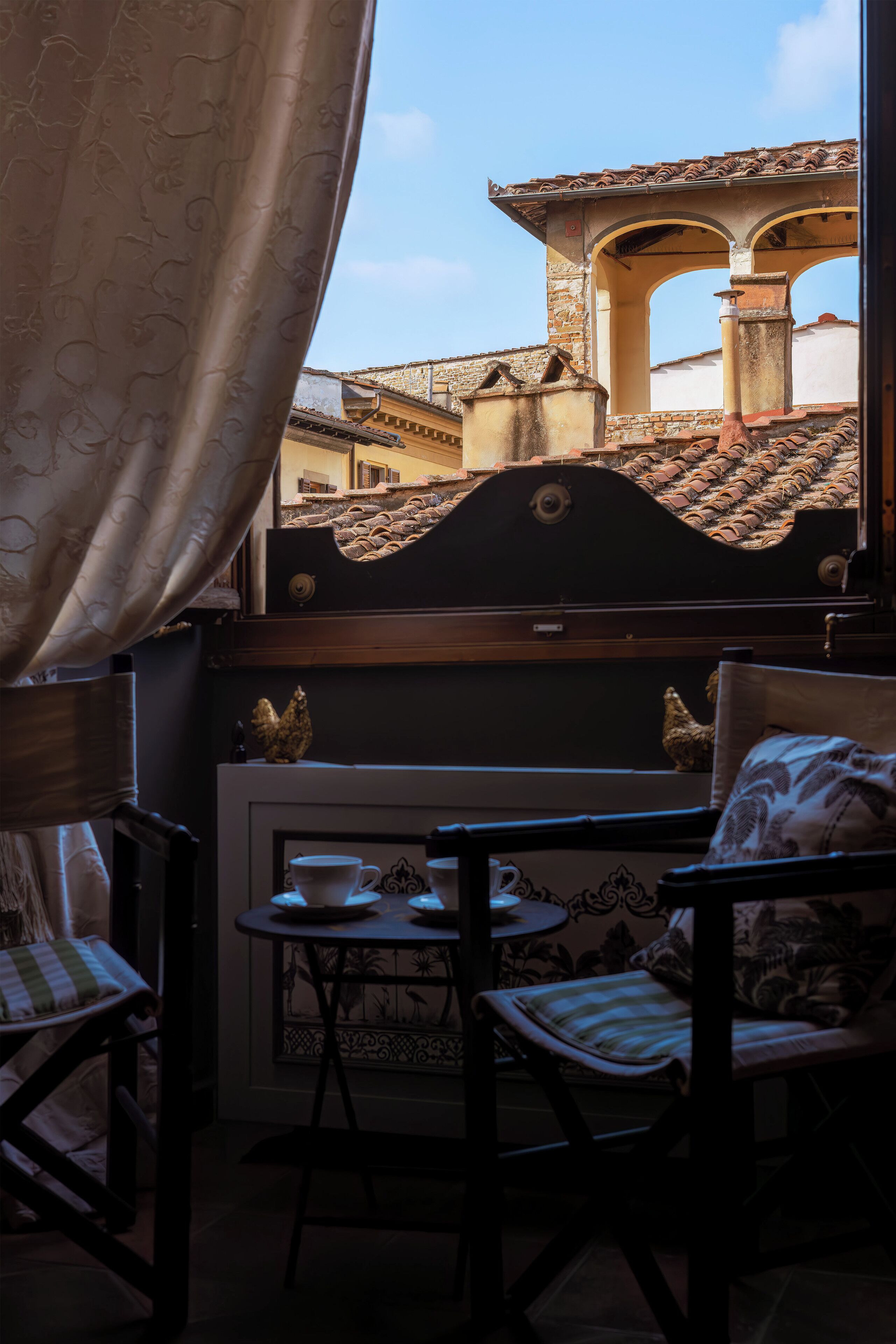 A room with a view of buildings, a table with cups, and two chairs.