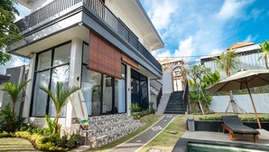 A modern house with a swimming pool, a covered outdoor area, and a staircase leading to a second floor.