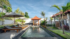 A pool area with lounge chairs, umbrellas, and a gazebo.