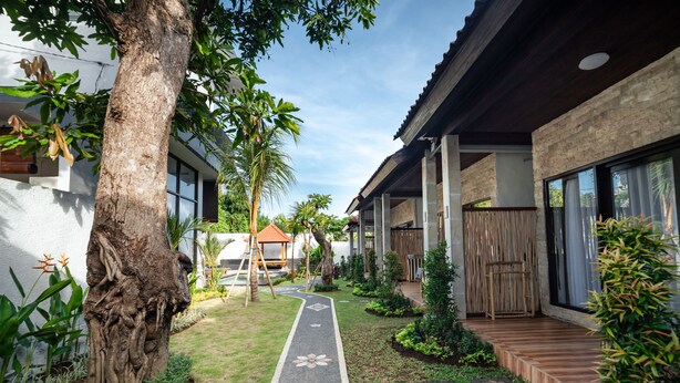 A pathway leading to a building with a covered porch, surrounded by greenery and a large tree.
