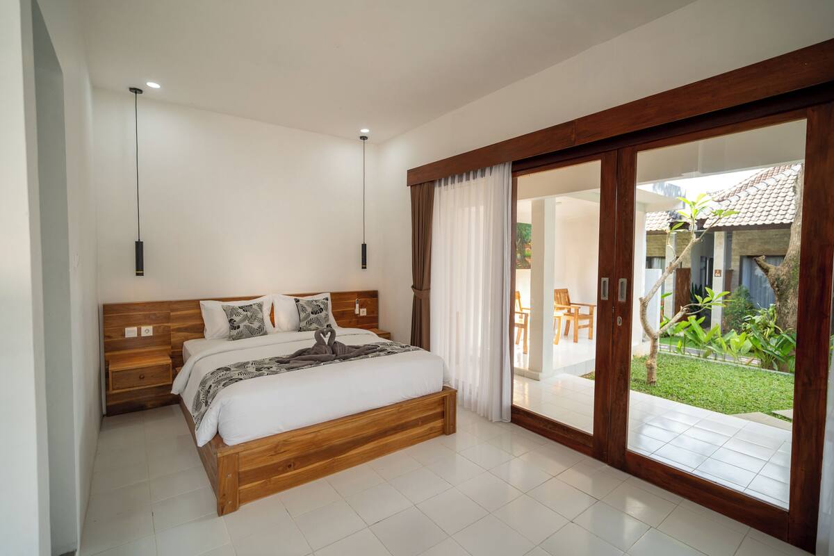A bedroom with a wooden bed, bedside tables, a large sliding glass door to a patio, and a ceiling light.