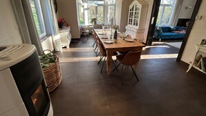 Een ruime eetruimte met een houten tafel, stoelen en een kroonluchter. Er is uitzicht op een tuin door grote ramen.