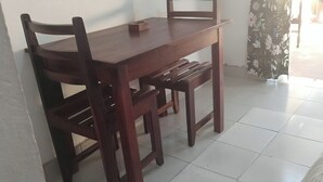A wooden dining table with chairs, positioned against a wall in a room with tiled flooring.