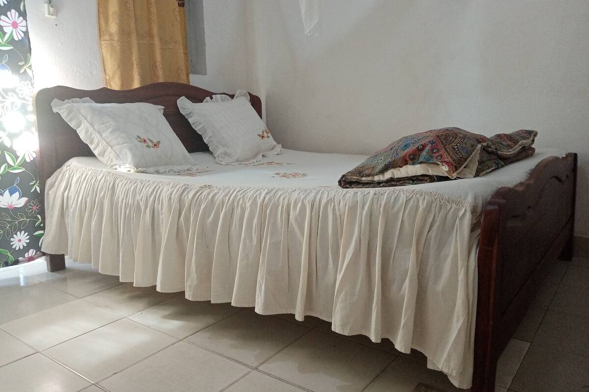 A bed with a white bedspread and pillows, a wooden headboard, and a patterned blanket.