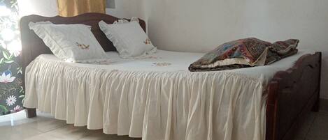 A bed with a white bedspread and pillows, a wooden headboard, and a patterned blanket.