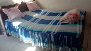 A bed with a striped bedspread and pillows, a window with curtains, and a tiled floor.