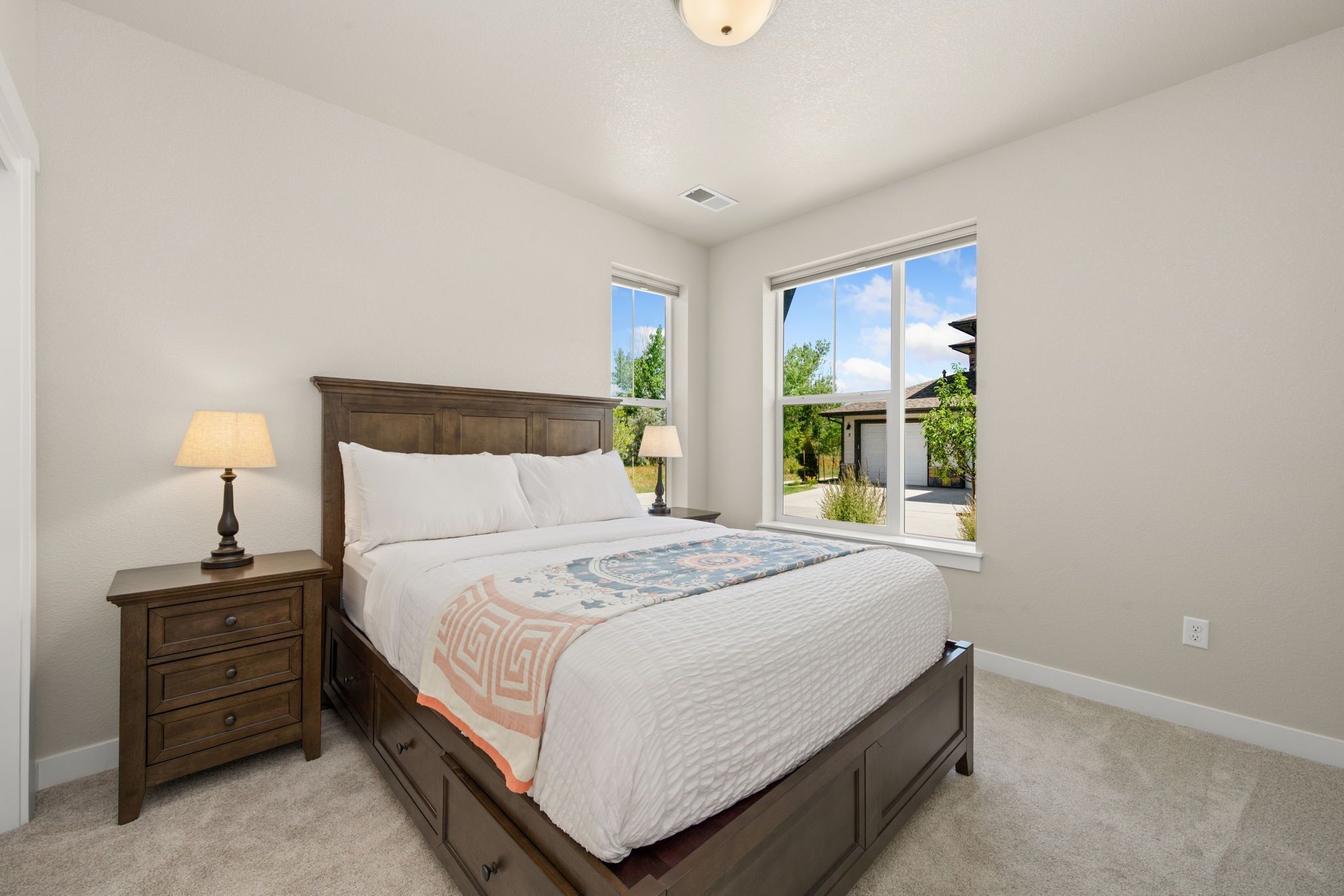 A bedroom with a bed, nightstand, and two windows.