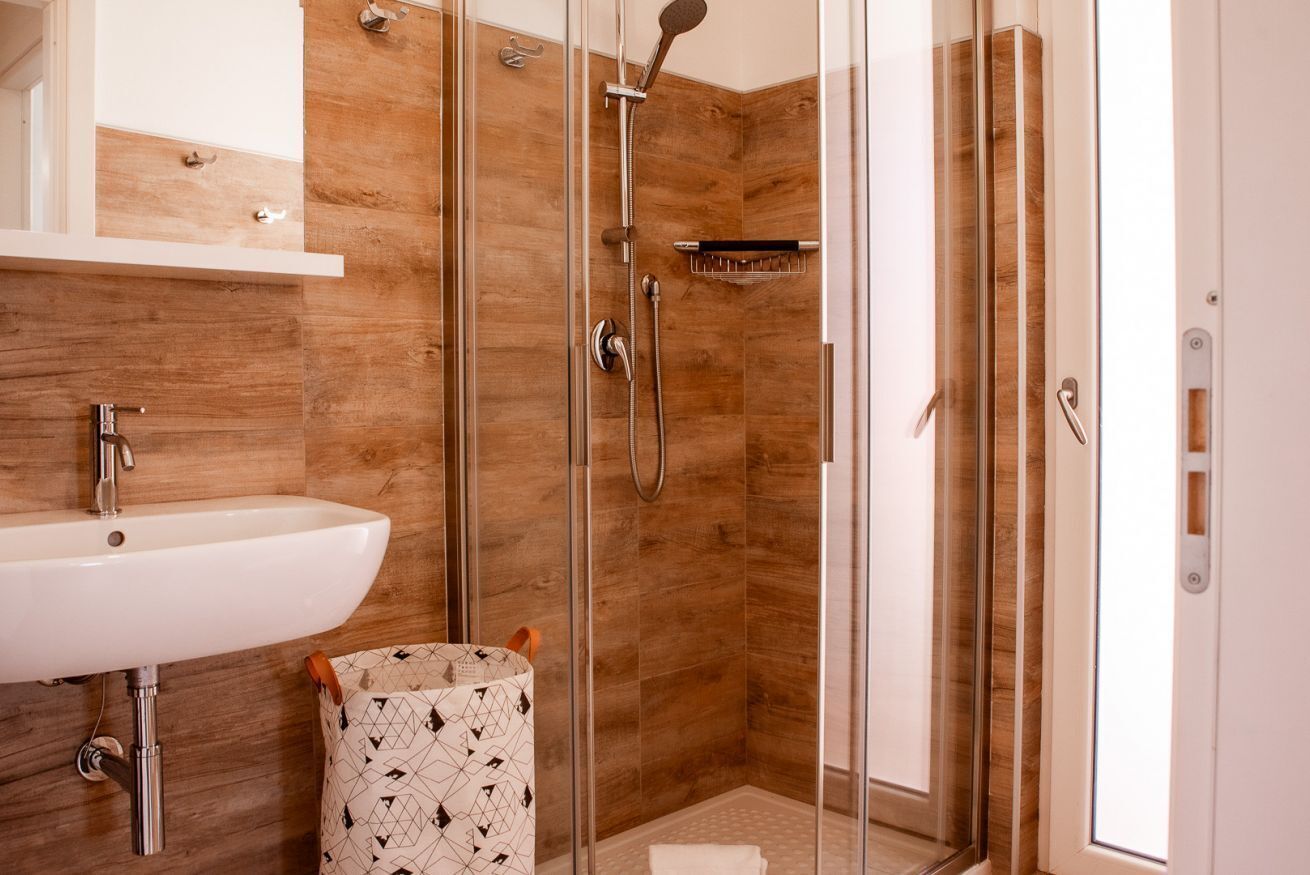 Uma casa de banho moderna com cabine de duche em vidro, lavatório branco e um contentor de lixo estampado.