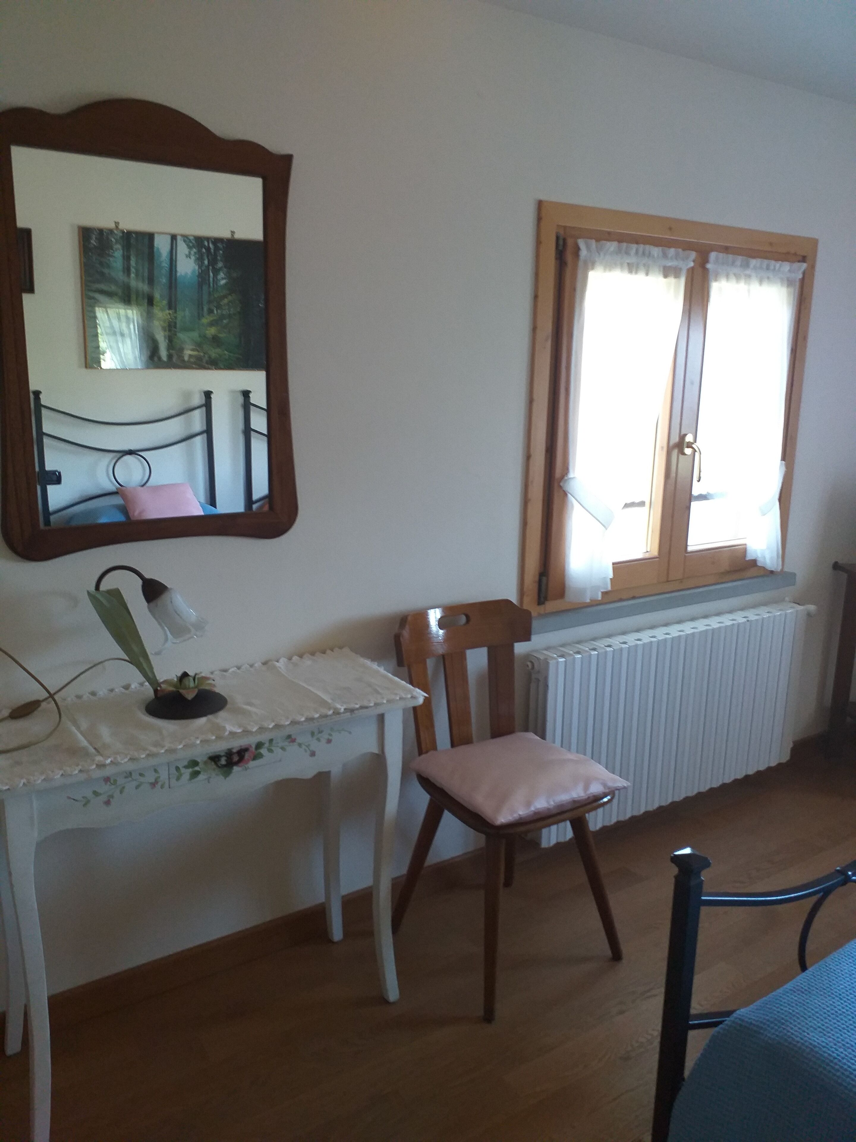 Een kamer met houten vloer, een wit bureau met spiegel, een stoel en een raam met gordijnen.