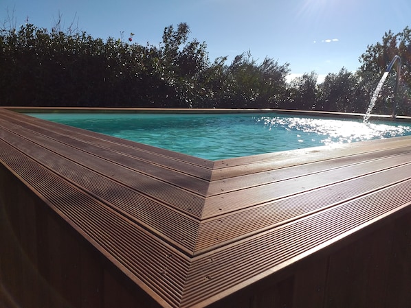 A wooden deck surrounding a swimming pool with a clear blue water surface.