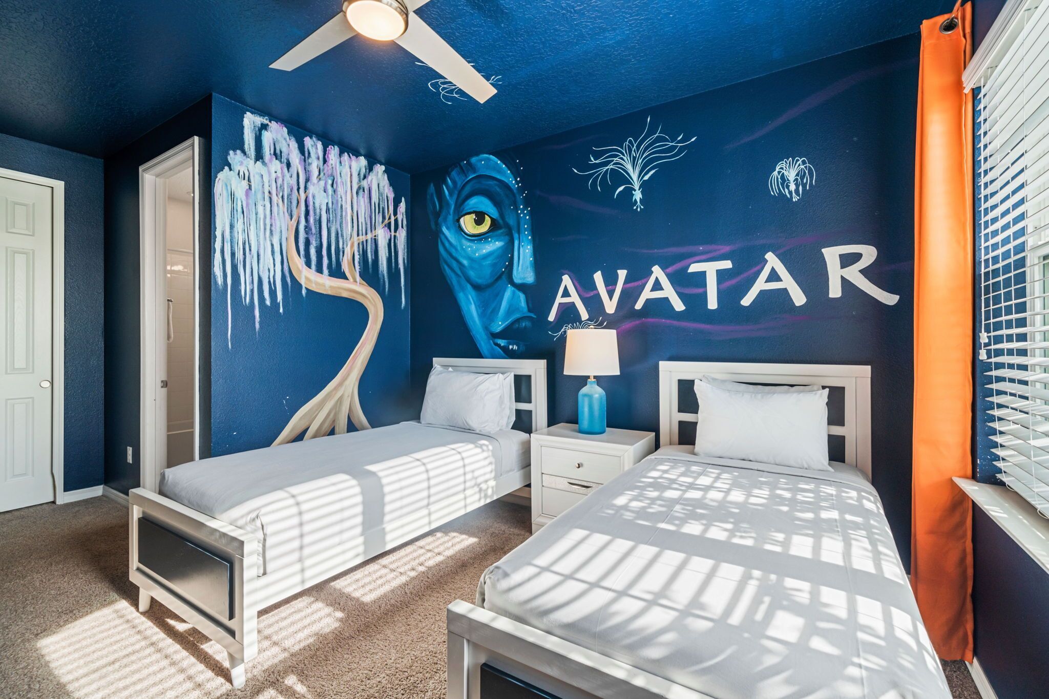 Et soveværelse med to senge, en loftsvifte og et vægmaleri med ordet "AVATAR".