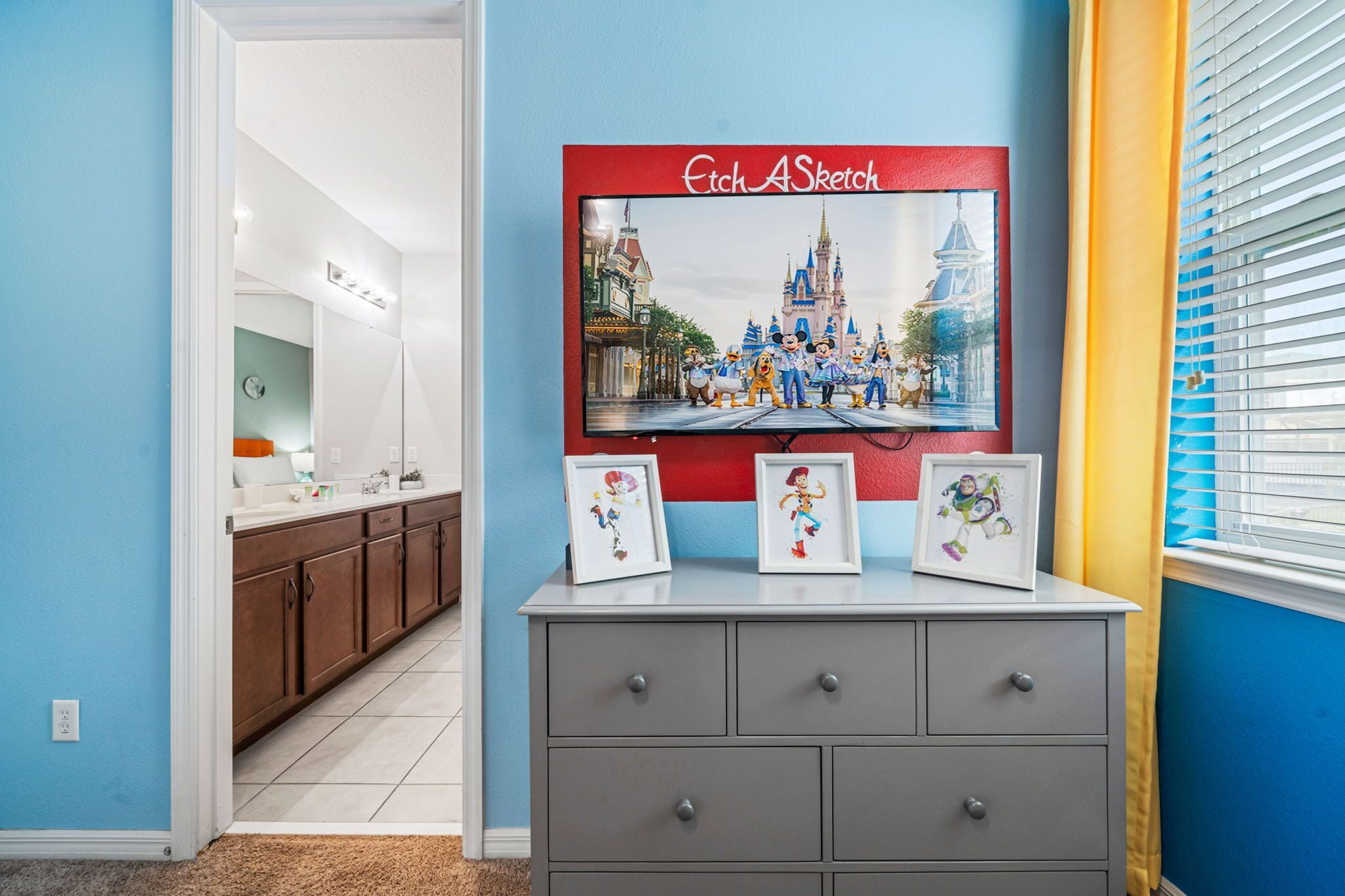 A hallway with a TV displaying a Disney-themed picture, a gray dresser with framed pictures, and a blue wall.