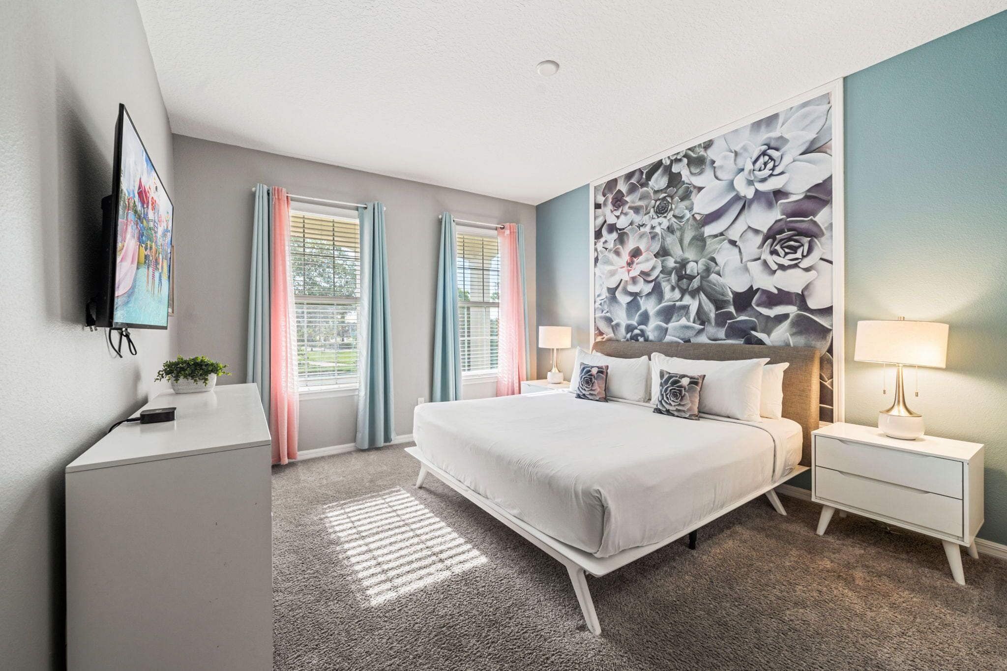 Une chambre moderne avec un grand lit, des tables de chevet, une télévision et une œuvre d’art florale accrochée au mur.