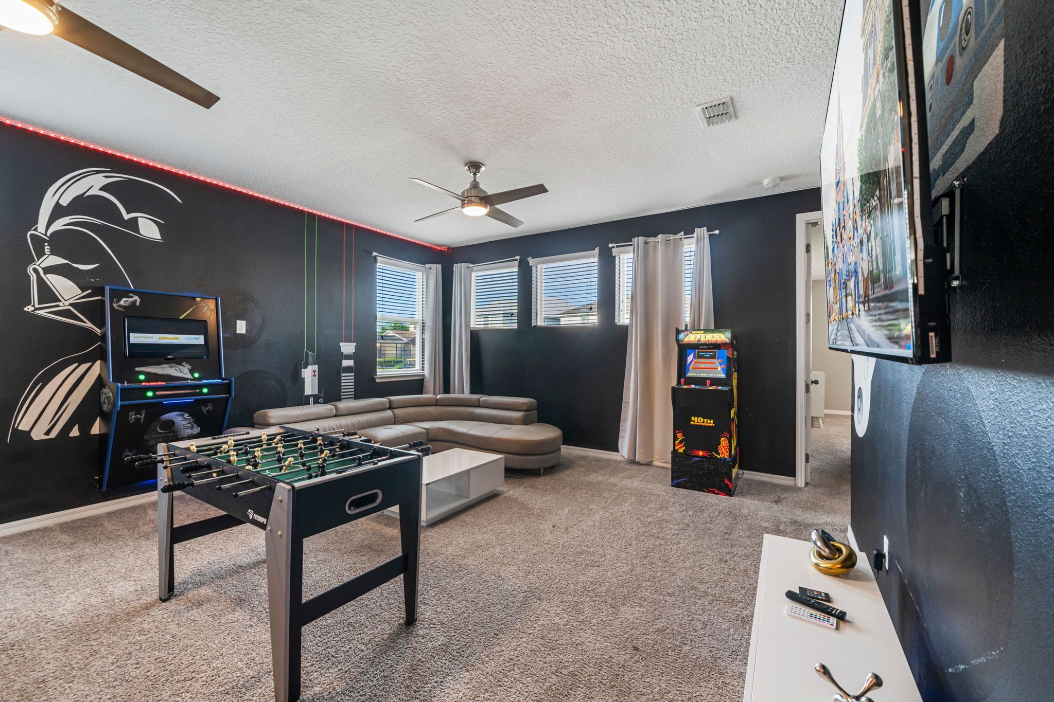 A living room with a foosball table, a ceiling fan, and a large TV.