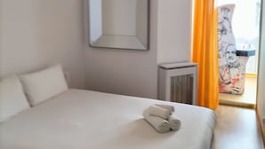 Une chambre d’hôtel avec un lit simple, un ventilateur de plafond, un radiateur et une fenêtre avec des rideaux orange.