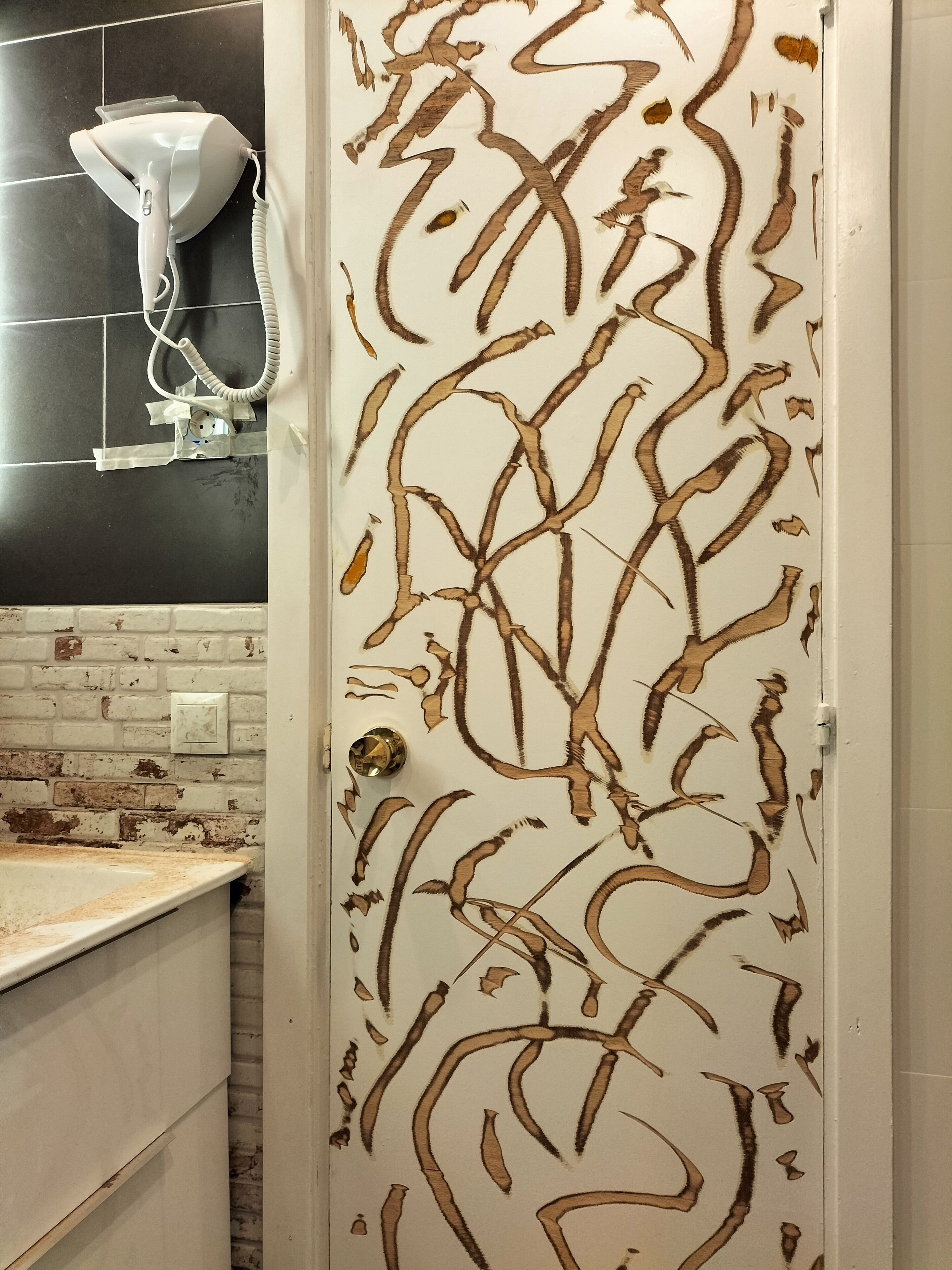 Ein Badezimmer mit einer weißen Tür, die ein einzigartiges abstraktes Design aufweist, einem weißen Waschbecken mit modernem Wasserhahn und einem an der Wand befestigten Fön.