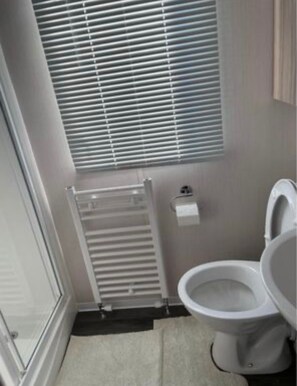 Une salle de bain avec des toilettes, un radiateur et une fenêtre équipée de stores.