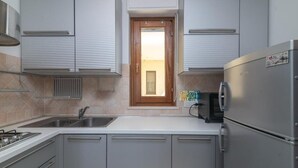 A modern kitchen with grey cabinets, a built-in oven, a stainless steel refrigerator, and a window with a wooden door.